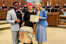 Female student in center holding artwork flanked by a man and a woman